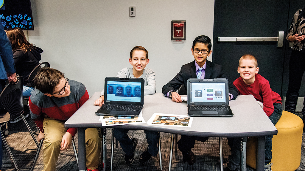 Four students show the camera their laptops and the AI projects on them