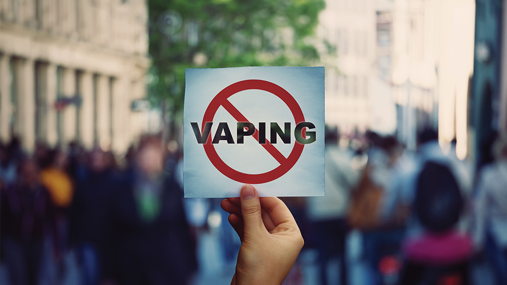 a hand holds up a sign that has the word "vaping" crossed out