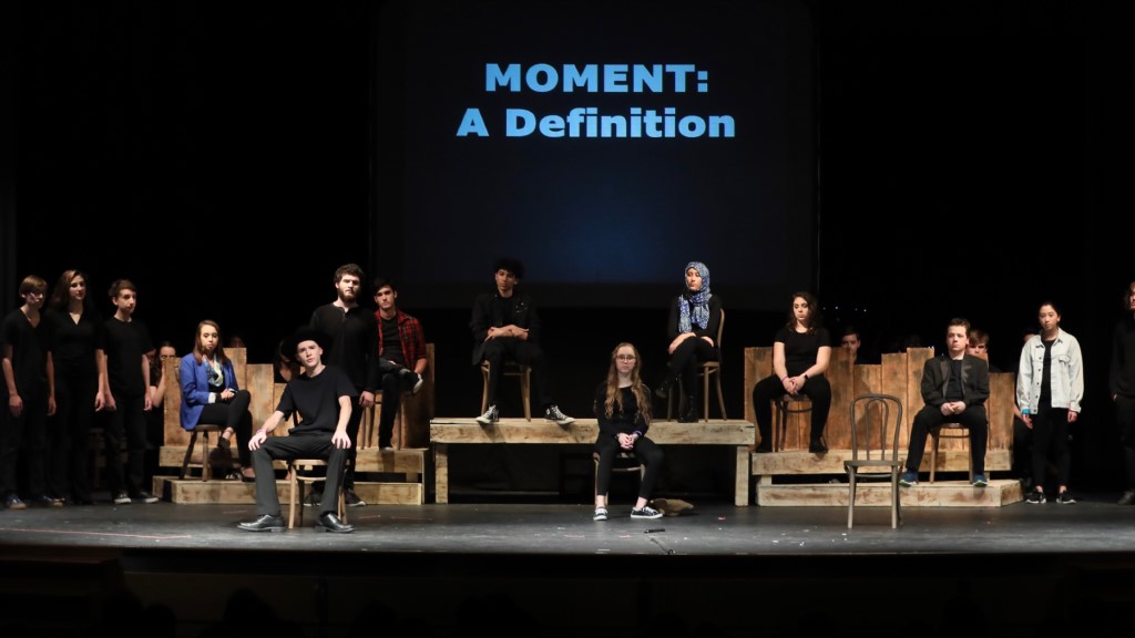 An entire cast of students stands on the stage, facing the audience