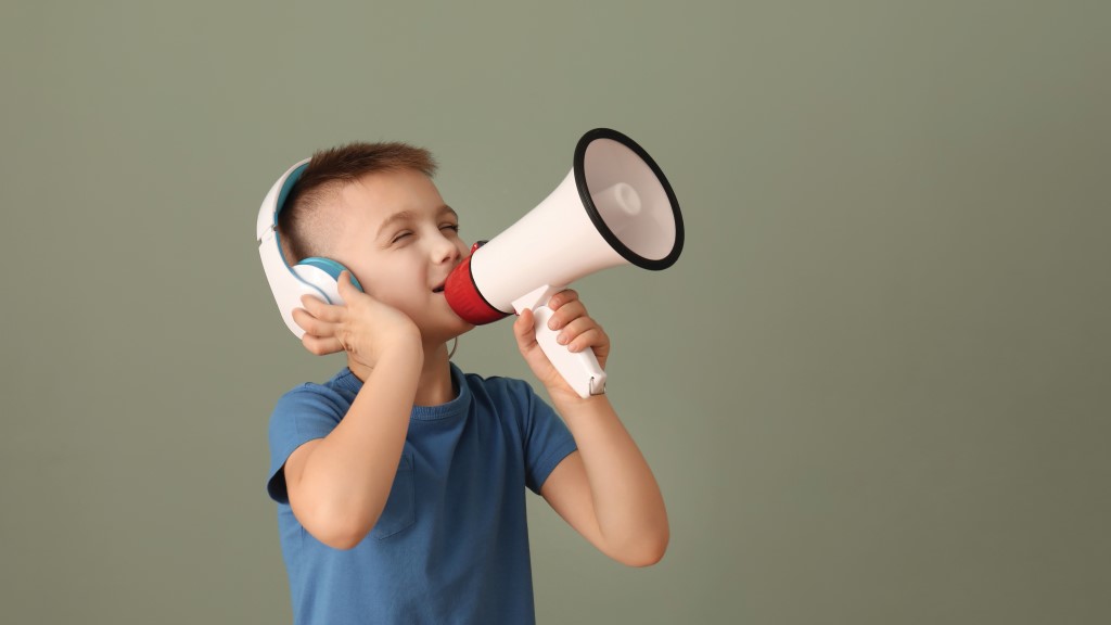 a boy wears headphones and speaks into a horn loudspeaker