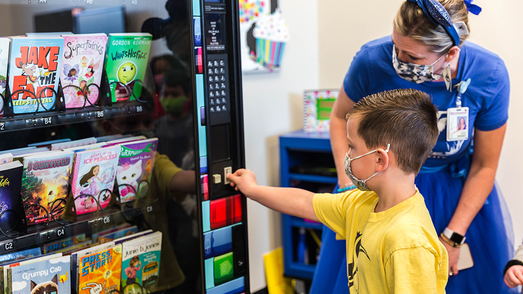 a student and teacher use a vending machine filled with books