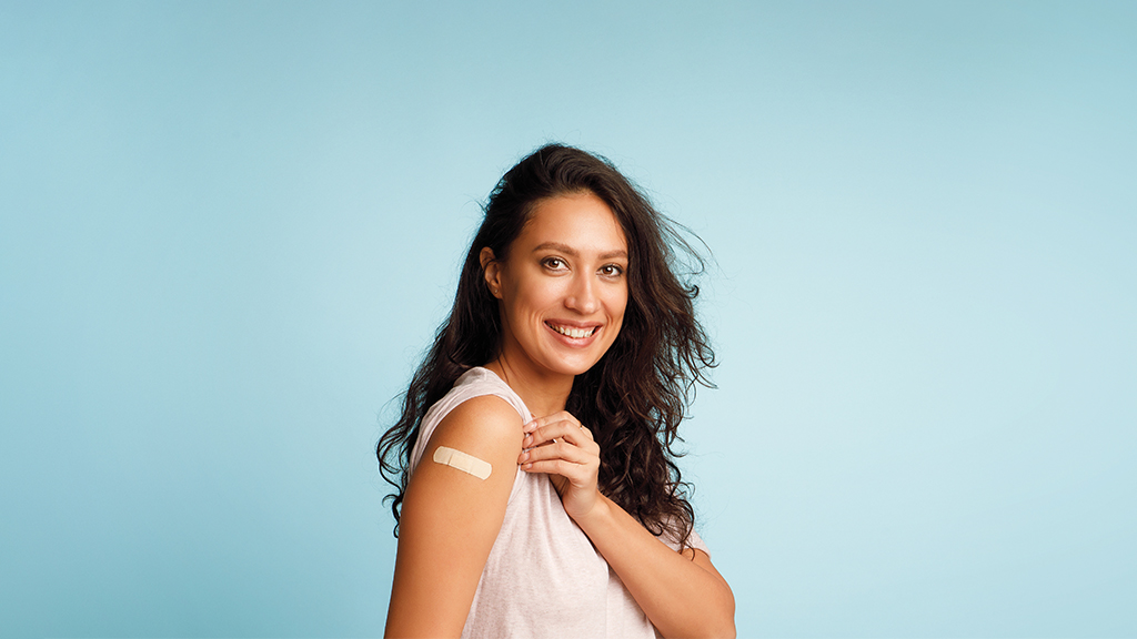 a woman smiles at the camera and shows the band aid placed on her upper arm