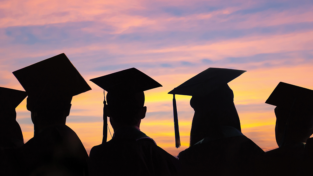 a silhouette of high school graduates wearing caps against a sunset