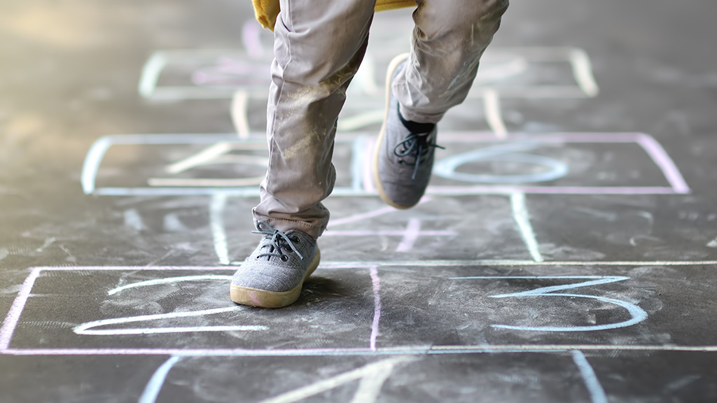 A child's feet hops across a hop scotch board etched in chalk on the ground