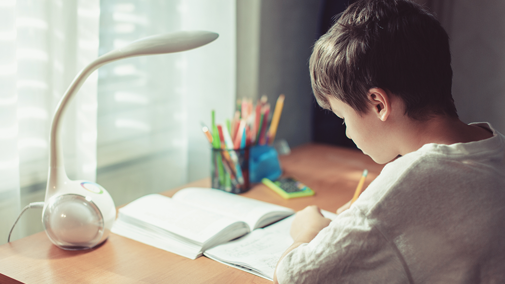 A boy sits at a desk at home doing schoolwork. 