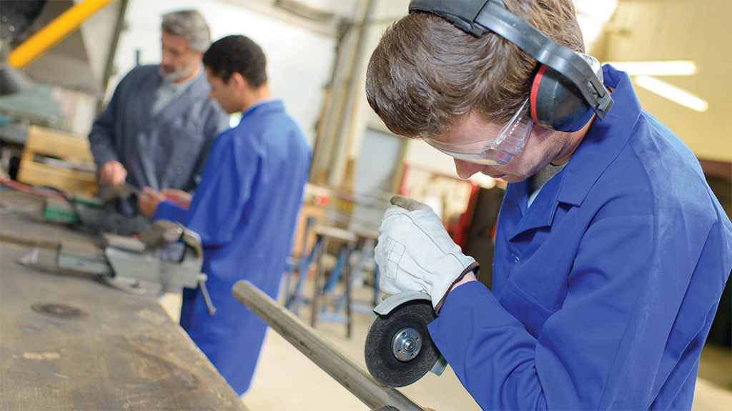 A teen boy uses equipment to cut a metal pole in a career and technical education class.