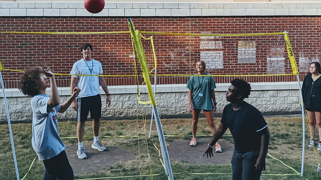 Two high school students play volleyball with two college mentors..