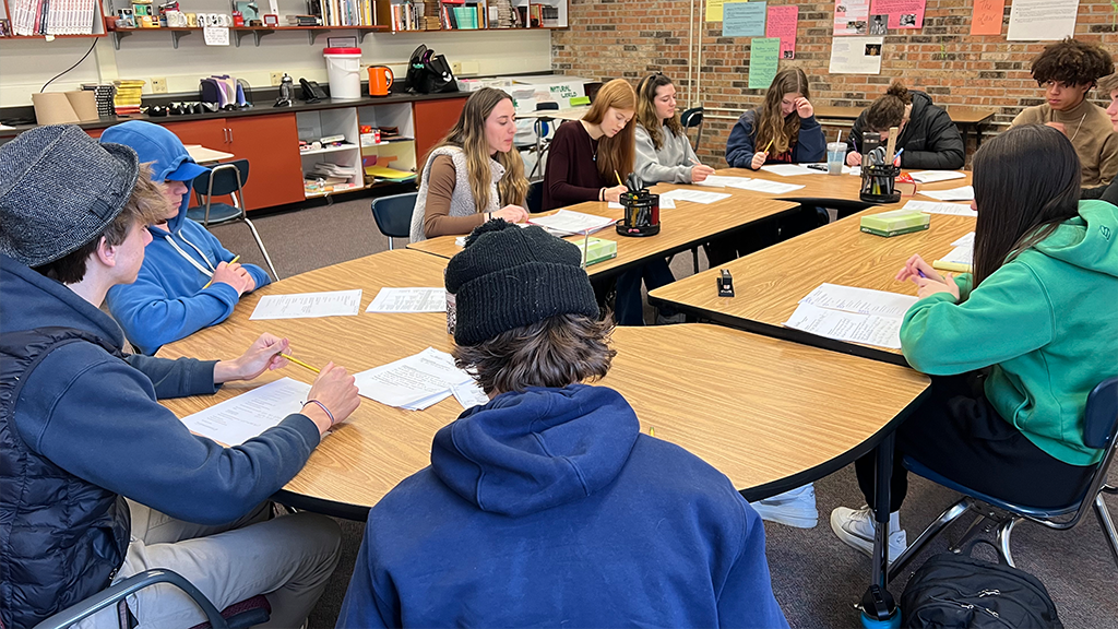 High school students sit around a conference table and engage in a discussion. 
