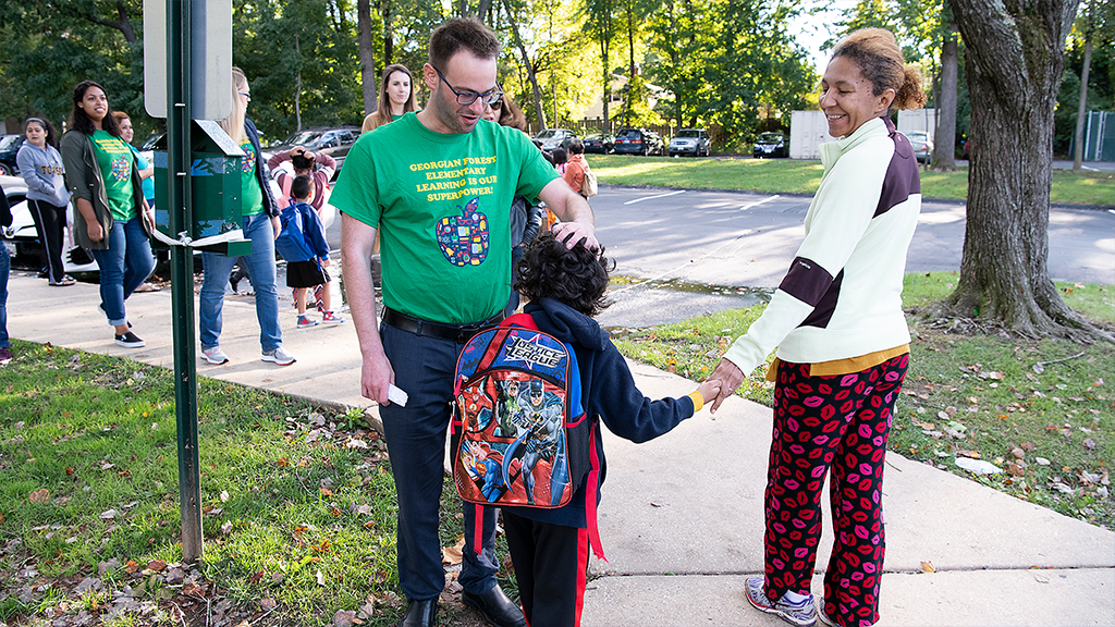 A teacher greets his student and the student's mother at the school bus stop.