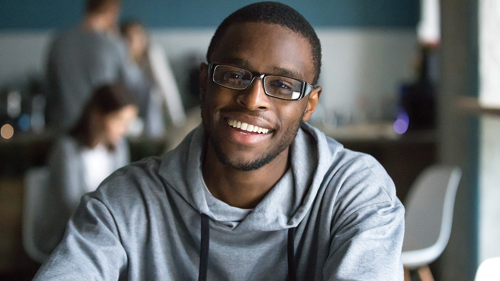 a teenage boy sits in a classroom and smiles at the camera