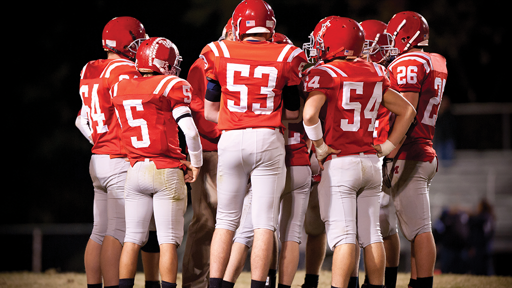 A group of high school football players dressed in their jerseys stand on a football field.