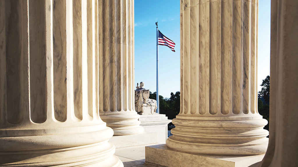 The United States Flag is seen through the columns of the U.S. Supreme Court