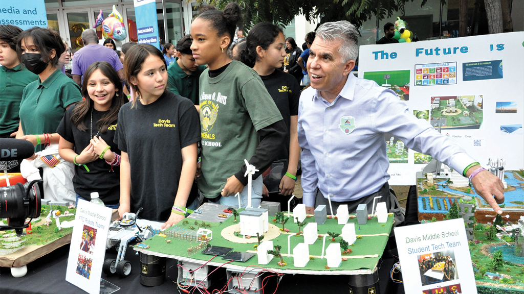 Students and their teacher show a model of a city development that they designed.