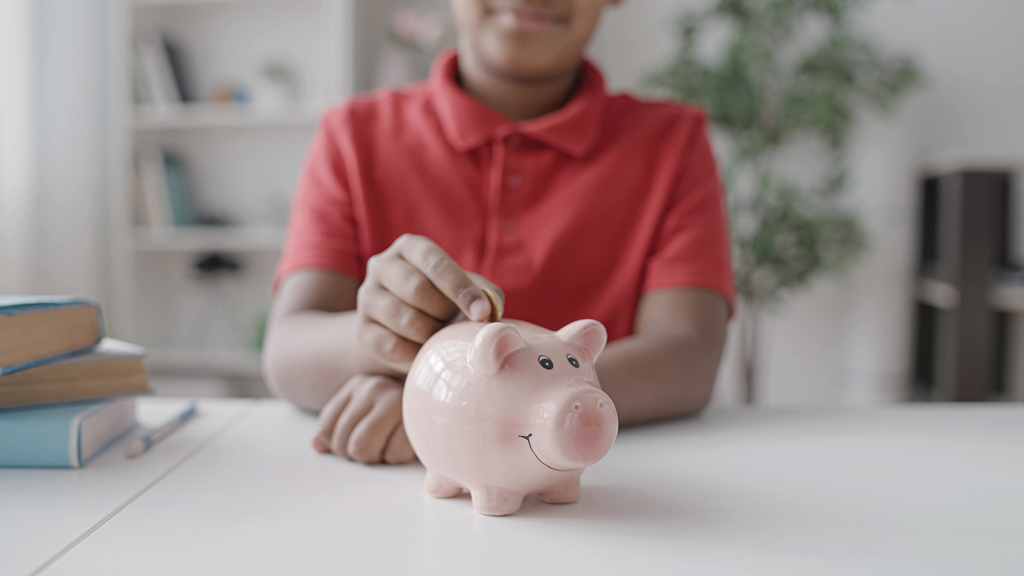 A boy drops a coin in a large piggy bank. 