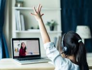 a girl, with her back toward the camera, raises her hand during remote learning